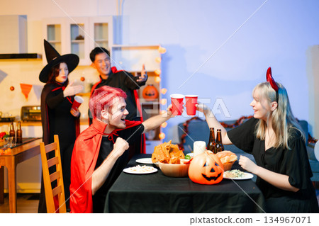 Group of young friends in Halloween costumes enjoy food and drinks at a cozy indoor party. with fun, spooky vibes, red cups, and pumpkin decor. Group of young friends in Halloween costumes enjoy food and drinks at a cozy indoor party. with fun, spooky vibes, red cups, and pumpkin decor. 134967071