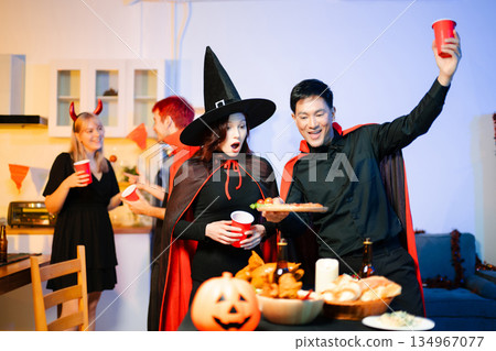 Young friends in Halloween costumes decorating pumpkin lanterns at a festive indoor party. Real people enjoying spooky vibes, red cups, snacks, and Halloween props. Young friends in Halloween costumes decorating pumpkin lanterns at a festive indoor party. Real people enjoying spooky vibes, red cups, snacks, and Halloween props. 134967077