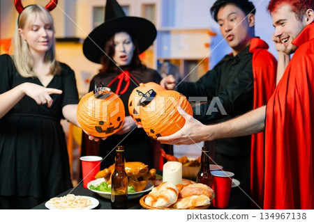 Group of friends in fun Halloween costumes laugh and play with spooky props, lanterns, and skull decor at a festive indoor party. Group of friends in fun Halloween costumes laugh and play with spooky props, lanterns, and skull decor at a festive indoor party. 134967138