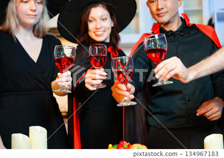 Halloween costumes toast with red wine at a festive indoor party. Pumpkins, food, and celebration set the mood for fun, spooky vibes and seasonal cheer. Halloween costumes toast with red wine at a festive indoor party. Pumpkins, food, and celebration set the mood for fun, spooky vibes and seasonal cheer. 134967183
