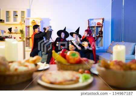 Halloween costumes toast with red wine at a festive indoor party. Pumpkins, food, and celebration set the mood for fun, spooky vibes and seasonal cheer. Halloween costumes toast with red wine at a festive indoor party. Pumpkins, food, and celebration set the mood for fun, spooky vibes and seasonal cheer. 134967187