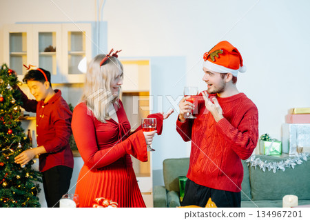Group of cheerful friends enjoying Christmas celebration with gifts, food, and holiday decorations in a warm festive atmosphere. Group of cheerful friends enjoying Christmas celebration with gifts, food, and holiday decorations in a warm festive atmosphere. 134967201