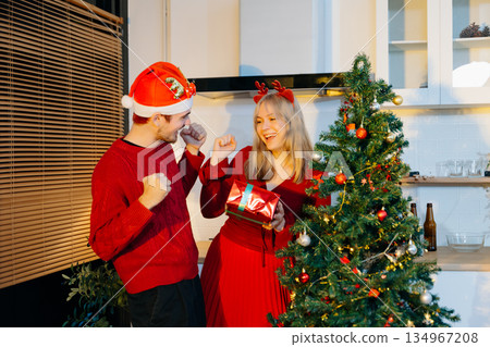 Smiling couple celebrating Christmas by exchanging gifts beside a decorated tree, sharing joy and festive holiday spirit in cozy indoor setting. Smiling couple celebrating Christmas by exchanging gifts beside a decorated tree, sharing joy and festive holiday spirit in cozy indoor setting. 134967208
