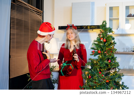 Smiling couple celebrating Christmas by exchanging gifts beside a decorated tree, sharing joy and festive holiday spirit in cozy indoor setting. Smiling couple celebrating Christmas by exchanging gifts beside a decorated tree, sharing joy and festive holiday spirit in cozy indoor setting. 134967212