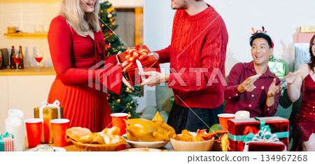 Friends celebrating Christmas together at a cozy home party with gift exchange, festive food and joyful holiday atmosphere. Friends celebrating Christmas together at a cozy home party with gift exchange, festive food and joyful holiday atmosphere. 134967268