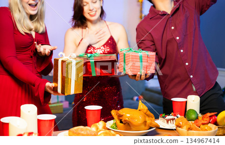 Holiday spirit with Asian friends exchanging gifts, sharing laughs, and enjoying a festive Christmas dinner in a cozy, joy filled setting. 134967414