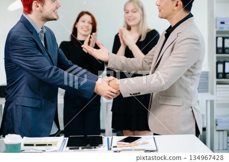 Successful business handshake with colleagues applauding, symbolizing teamwork, partnership, trust, and corporate achievement in a modern office 134967428