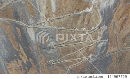 Aerial view of winding dirt roads through rugged mountainous terrain Aerial view of winding dirt roads through rugged mountainous terrain 134967739
