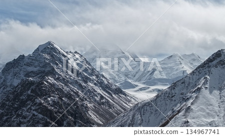 Snow-covered mountain peaks under cloudy sky with dramatic landscape 134967741