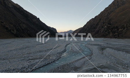 Serene river winding through rocky valley at dusk with mountains in background Serene river winding through rocky valley at dusk with mountains in background 134967755