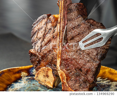 Juicy grilled tomahawk steak sliced with knife and fork on dark background Juicy grilled tomahawk steak sliced with knife and fork on dark background 134969290