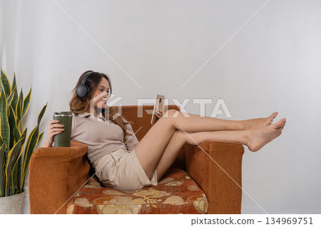 Caucasian woman listening to music with headphones, legs up Caucasian woman listening to music with headphones, legs up 134969751