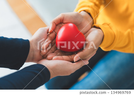 Closeup view of red heart on woman and man hands. Healthy and valentines day concept Closeup view of red heart on woman and man hands. Healthy and valentines day concept 134969769