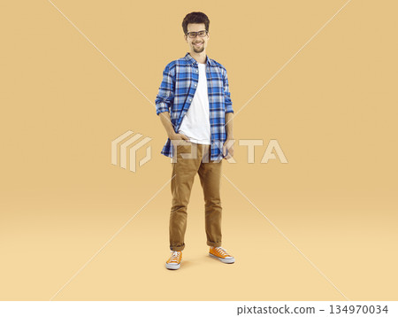 Portrait of a happy male student in glasses and casual clothes standing on a studio background 134970034