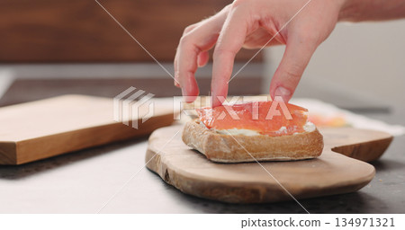 man hands put smoked salmon on ciabatta with cream cheese to make a sandwich on wood board 134971321