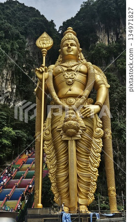Lord Murugan golden statue stands majestically before rainbow stairs and limestone cliffs, radiating spiritual grandeur, cultural pride, and natural beauty at Malaysia iconic Batu Caves temple. Lord Murugan golden statue stands majestically before rainbow stairs and limestone cliffs, radiating spiritual grandeur, cultural pride, and natural beauty at Malaysia iconic Batu Caves temple. 134971827