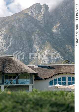 Luxurious thatched roof building nestled at foot of rugged mountain Luxurious thatched roof building nestled at foot of rugged mountain 134972384