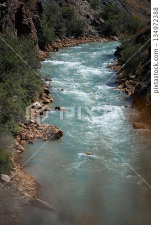 Clear blue river flows rapidly through a rocky valley with green vegetation Clear blue river flows rapidly through a rocky valley with green vegetation 134972388