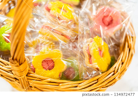 Colorful flower-shaped Easter cookie sandwiches with raspberry buttercream filling, individually wrapped and arranged in a wicker basket. Perfect for spring gifting, Easter parties, and festive Colorful flower-shaped Easter cookie sandwiches with raspberry buttercream filling, individually wrapped and arranged in a wicker basket. Perfect for spring gifting, Easter parties, and festive 134972477