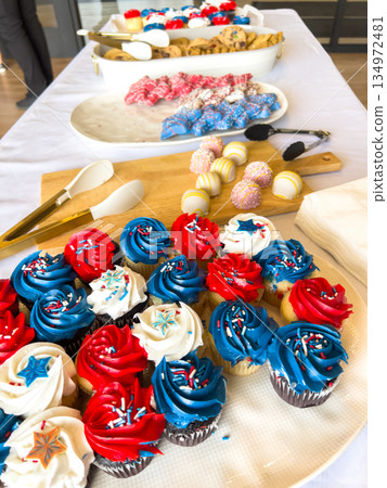 Wide view of a dessert table featuring red, white, and blue cupcakes alongside other colorful sweets. The setup is festive and brightly lit, suggesting a party or holiday event. Wide view of a dessert table featuring red, white, and blue cupcakes alongside other colorful sweets. The setup is festive and brightly lit, suggesting a party or holiday event. 134972481