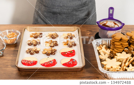 Skillfully decorating cookies with vibrant red melted chocolate and a generous sprinkle of vibrant green, creating a festive holiday treat. Skillfully decorating cookies with vibrant red melted chocolate and a generous sprinkle of vibrant green, creating a festive holiday treat. 134972488
