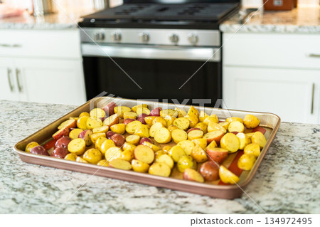 In a modern kitchen, an array of halved, multicolored marble potatoes are arranged on a baking pan lined with a silicone liner. The roasting process infuses the kitchen with a mouthwatering aroma In a modern kitchen, an array of halved, multicolored marble potatoes are arranged on a baking pan lined with a silicone liner. The roasting process infuses the kitchen with a mouthwatering aroma 134972495