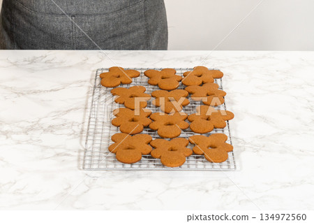 Front-facing view of a cooling rack filled with an even arrangement of gingerbread man cookies, showcasing their festive design and baked texture. Front-facing view of a cooling rack filled with an even arrangement of gingerbread man cookies, showcasing their festive design and baked texture. 134972560