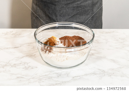 Person in apron holding a glass bowl filled with flour, cinnamon, ginger, and other spices for Pale Gingerbread Cookies with Subtle Spice Flavor. Ingredients are ready for mixing. Person in apron holding a glass bowl filled with flour, cinnamon, ginger, and other spices for Pale Gingerbread Cookies with Subtle Spice Flavor. Ingredients are ready for mixing. 134972568