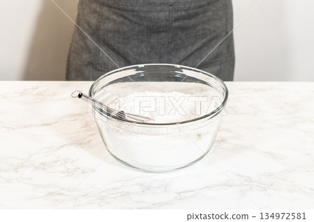 A whisk placed in a glass mixing bowl containing sifted powdered sugar, ready for the preparation of Simple White Royal Icing. 134972581