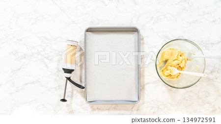 Piped lemon spritz cookie dough on a baking tray next to a bowl of remaining dough. A cookie press is visible, showing the preparation process before baking. 134972591