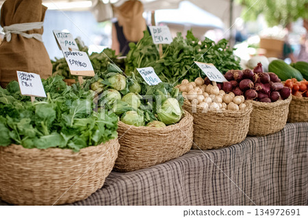 Fresh leafy greens, white mushrooms, red onions, and lettuce arranged in wicker baskets on a plaid market table. Handwritten signs add a rustic, artisanal vibe. Excellent for farmers market promotions 134972691