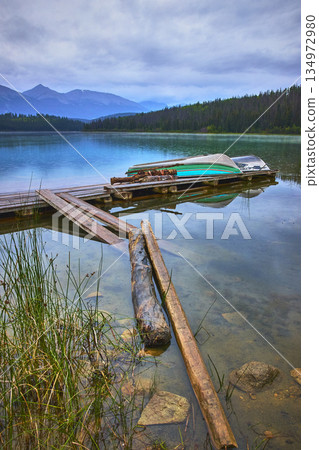 Rustic Wooden Dock and Canoes on Serene Mountain Lake with Forest Reflections Rustic Wooden Dock and Canoes on Serene Mountain Lake with Forest Reflections 134972980
