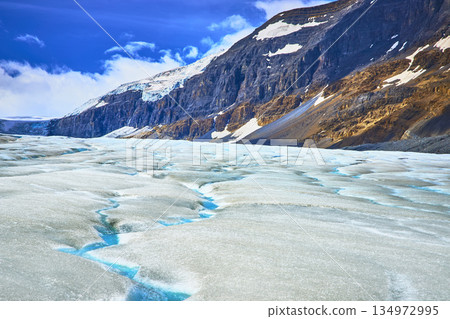 Athabasca Glacier Crevasses and Rocky Mountain Slopes Under Blue Sky 134972995