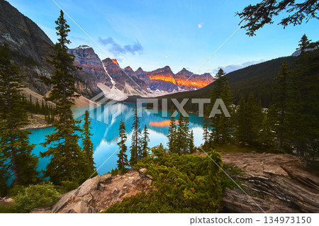 Lake Moraine Sunrise Reflection with Blue Water and Mountain Peaks in Forest Landscape 134973150