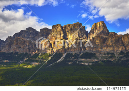 Majestic Rocky Mountain Cliffs Sunlit Forest and Dramatic Blue Sky in Banff Canada 134973155