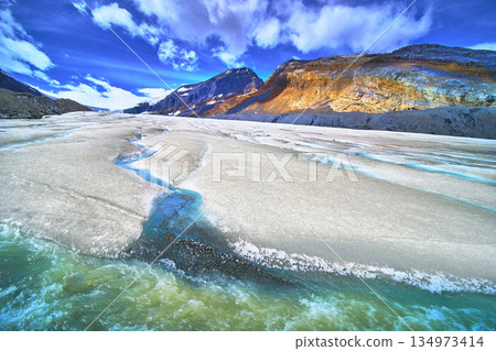 Athabasca Glacier Meltwater Flow and Rocky Mountain Landscape Under Vibrant Sky 134973414