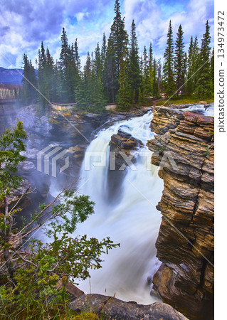 Athabasca Falls Waterfall Cascading Through Rocky Cliffs and Evergreen Forest Athabasca Falls Waterfall Cascading Through Rocky Cliffs and Evergreen Forest 134973472