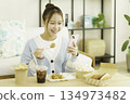 一位年輕的日本女性在客廳裡一邊吃午餐一邊看著她的智慧型手機。 134973482