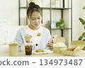 一位年輕的日本女性在客廳一邊吃著便當，一邊看著手機，擔心著卡路里。 134973487