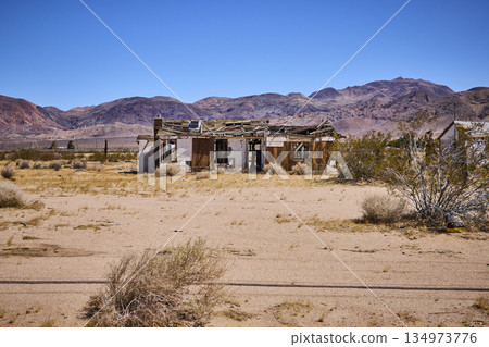 Abandoned Desert Building With Collapsed Roof And Mountain Range Under Blue Sky Abandoned Desert Building With Collapsed Roof And Mountain Range Under Blue Sky 134973776