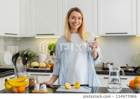 Young woman squeezing lemon into water tumbler in kitchen for fresh vitamin hydration morning habit Young woman squeezing lemon into water tumbler in kitchen for fresh vitamin hydration morning habit 134973966