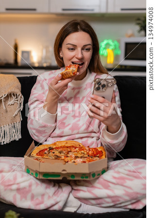 Adult woman eats pizza and messages friend on smartphone at night smiles cozy vibe social chat happy Adult woman eats pizza and messages friend on smartphone at night smiles cozy vibe social chat happy 134974008