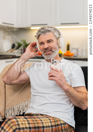 Middle-aged man listens to favorite music with headphones nods to rhythm smiles rests during break Middle-aged man listens to favorite music with headphones nods to rhythm smiles rests during break 134974015