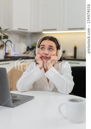 Young woman in headphones thinking with laptop leans on hands worried decision responsibility mind Young woman in headphones thinking with laptop leans on hands worried decision responsibility mind 134974016