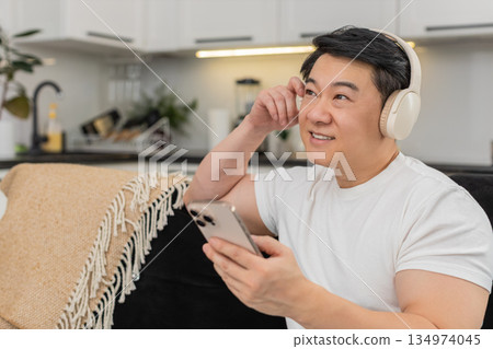 Asian man with wireless headphones enjoys playlist relaxes closes eyes rocks gently and smiles calm 134974045