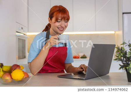 Young woman in kitchen with laptop replies to emails takes coffee sip and manages tasks with focus Young woman in kitchen with laptop replies to emails takes coffee sip and manages tasks with focus 134974062