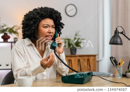 African American businesswoman yells on retro phone waving hand frustrated during angry dispute call 134974087