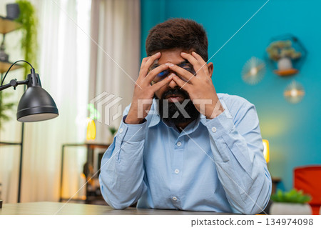 Indian man buries face in palms feeling burnout stressed severe emotional exhaustion moment indoors Indian man buries face in palms feeling burnout stressed severe emotional exhaustion moment indoors 134974098