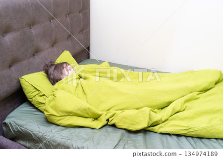 Young child sleeping soundly in a cozy bed. Kid resting under a warm green duvet 134974189