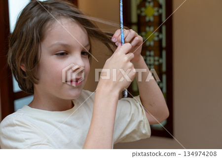 Young boy styling his brown hair with a pencil at home. Candid childhood portrait Young boy styling his brown hair with a pencil at home. Candid childhood portrait 134974208